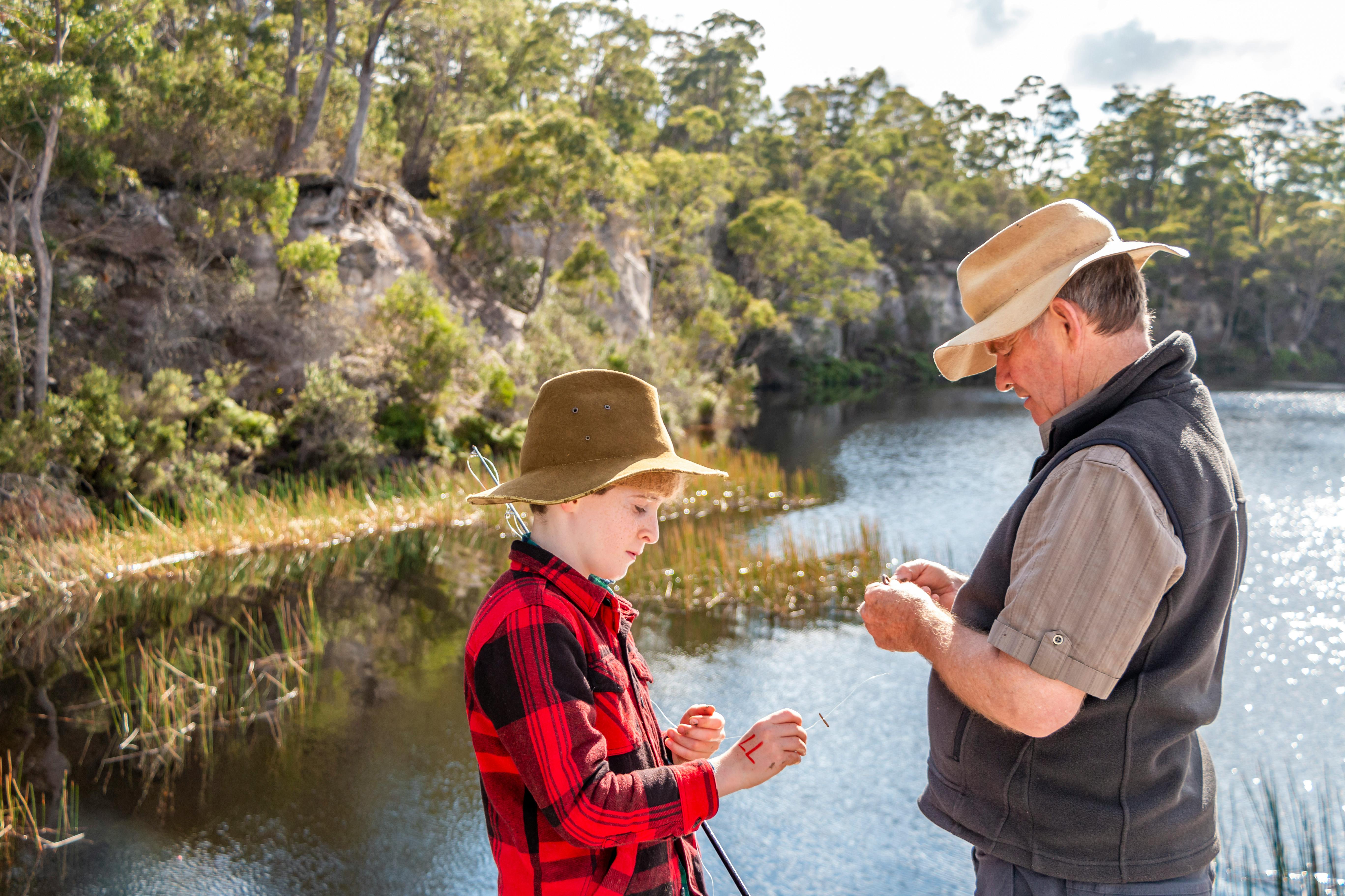 A parent and child fishing together near calm coastal water.